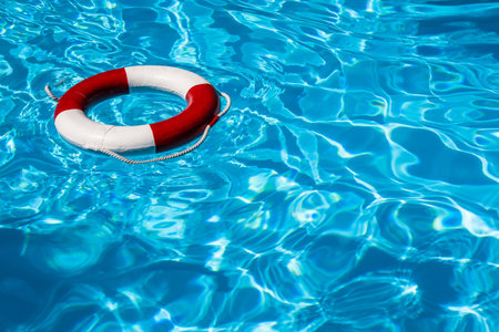 A close up shot of a life guards red and white rescue ring buoy floating in a pool 