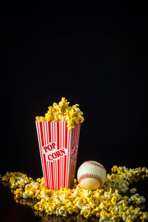 A close up shot of a classic box of red and white striped popcorn box with a baseball isolated against a black background.の写真素材