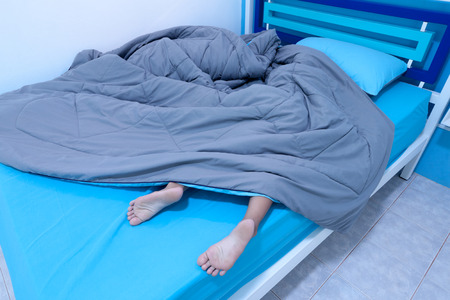 Child sleep in bed with Legs sticking out from under the blanket in the bedroomの写真素材