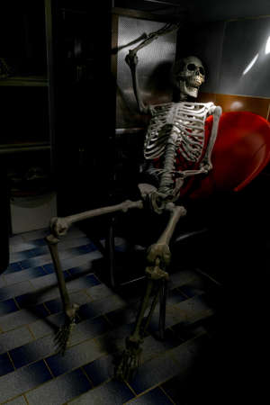 Fake human skeleton sitting on the chair in dark room.の写真素材