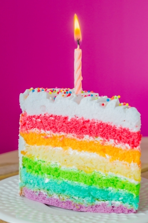 Rainbow cake with candle on white dishの写真素材