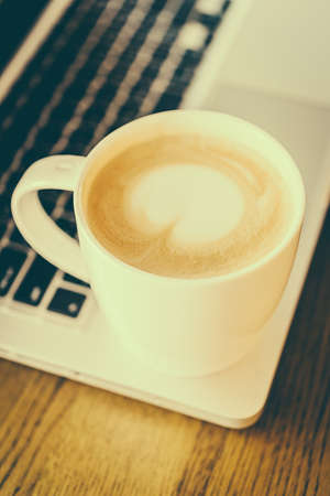 Hot latte coffee cup and laptob in coffee shop - vintage effect style picturesの写真素材