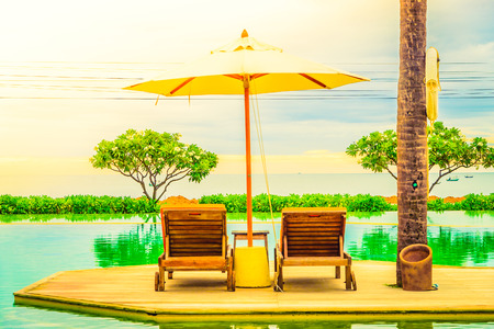 Umbrella chair in hotel pool resort with sunset - Vintage filter and sunflare light filter processingの写真素材