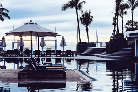 Silhouette palm tree with umbrella and chair in the luxury hotel pool resort at sunrise times - Vintage filter processing style picturesのeditorial素材
