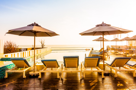 Beautiful luxury swimming pool in hotel resort with umbrella and chair in sunset times - Vintage...
