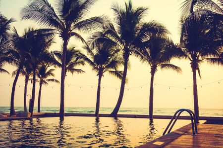 Silhouette palm tree on the beach and sea around beautiful luxury swimming pool in sunset - Vintage Filter and Boost up color Processingのeditorial素材