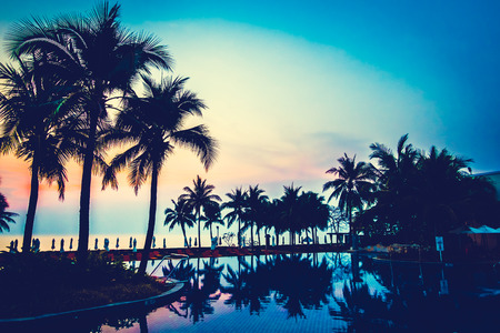 Silhouette palm tree with umbrella and chair around beautiful luxury swimming pool in hotel resort...