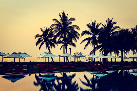 Silhouette palm tree with umbrella and chair around beautiful luxury swimming pool in hotel resort at Sunset time - Vintage Filter and Boost up Color Processingのeditorial素材
