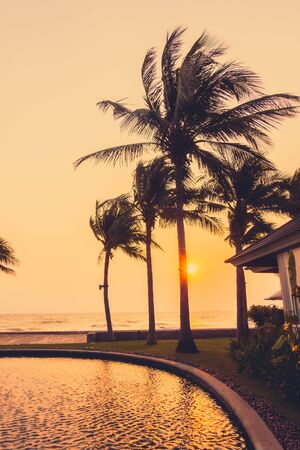 Silhouette palm tree on the beach and sea around beautiful luxury swimming pool in sunset - Vintage Filter and Boost up color Processingの写真素材