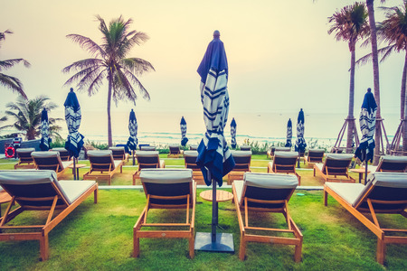 Beautiful luxury outdoor swimming pool in hotel resort with silhouette umbrella and chair and coconut palm tree - Vintage Filter and Boost up color Processingのeditorial素材