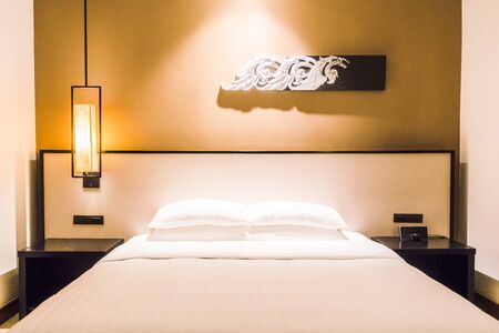 Beautiful luxury White pillow on bed and light lamp on wall decoration in bedroom interior - Vintage Light Filterの写真素材