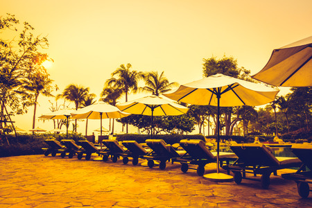 Beautiful Silhouette luxury umbrella and chair around swimming pool in hotel pool resort with coconut palm tree at sunrise times - Vintage Filter and Boost up color Processingのeditorial素材