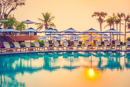 Beautiful luxury outdoor swimming pool in hotel resort with silhouette umbrella and chair and coconut palm tree - Vintage Filter and Boost up color Processingの写真素材