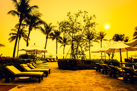 Beautiful Silhouette luxury umbrella and chair around swimming pool in hotel pool resort with coconut palm tree at sunrise times - Vintage Filter and Boost up color Processingの写真素材