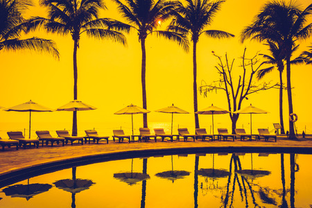 Beautiful Silhouette luxury umbrella and chair around swimming pool in hotel pool resort with coconut palm tree at sunrise times - Vintage Filter and Boost up color Processingのeditorial素材