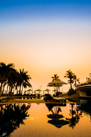 Beautiful Silhouette palm tree with umbrella and chair around luxury swimming pool in hotel resort at sunset time - Vintage Filter and Color boost Up Processingのeditorial素材