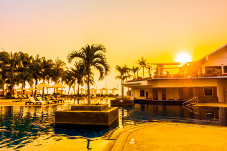 Beautiful Silhouette palm tree with umbrella and chair around luxury swimming pool in hotel resort...