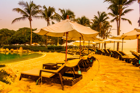 Beautiful Silhouette luxury umbrella and chair around swimming pool in hotel pool resort with coconut palm tree at sunrise times - Vintage Filter and Boost up color Processingのeditorial素材