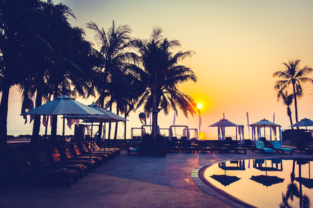 Beautiful Silhouette palm tree with umbrella and chair around luxury swimming pool in hotel resort at sunset time - Vintage Filter and Color boost Up Processingのeditorial素材