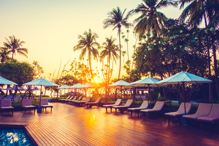 Silhouette coconut palm tree with umbrella and chair at sunrise time around outdoor swimming pool in hotel resort - Vintage filterのeditorial素材