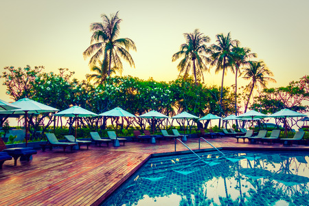 Silhouette coconut palm tree with umbrella and chair at sunrise time around outdoor swimming pool in hotel resort - Vintage filterのeditorial素材