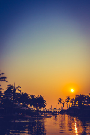 Beautiful Silhouette palm tree with umbrella and chair around luxury swimming pool in hotel resort at sunset time - Vintage Filter and Color boost Up Processingのeditorial素材
