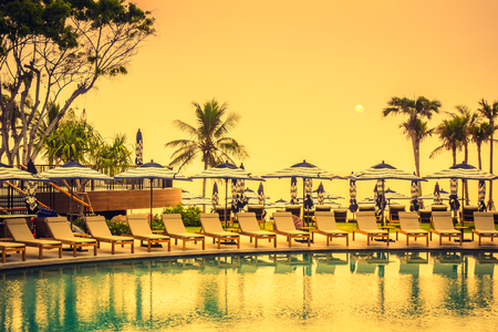 Beautiful luxury outdoor swimming pool in hotel resort with silhouette umbrella and chair and coconut palm tree - Vintage Filter and Boost up color Processingのeditorial素材