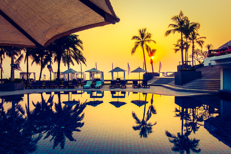 Beautiful Silhouette palm tree with umbrella and chair around luxury swimming pool in hotel resort at sunset time - Vintage Filter and Color boost Up Processingのeditorial素材