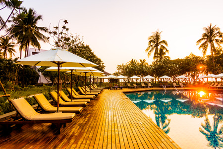 Silhouette coconut palm tree with umbrella and chair at sunrise time around outdoor swimming pool in...