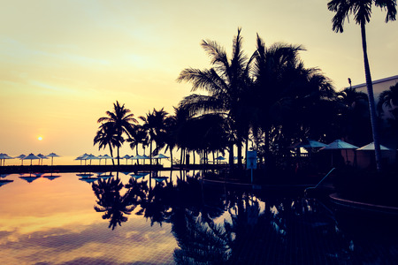 Silhouette palm tree with umbrella and chair around beautiful luxury swimming pool in hotel resort at Sunset time - Vintage Filter and Boost up Color Processingのeditorial素材
