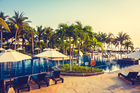 Beautiful Silhouette palm tree with umbrella and chair around luxury swimming pool in hotel resort at sunset time - Vintage Filter and Color boost Up Processingのeditorial素材