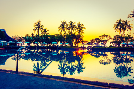 Silhouette coconut palm tree with umbrella and chair at sunrise time around outdoor swimming pool in hotel resort - Vintage filterのeditorial素材