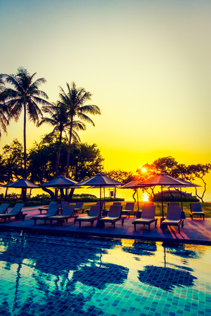 Silhouette coconut palm tree with umbrella and chair at sunrise time around outdoor swimming pool in hotel resort - Vintage filterのeditorial素材
