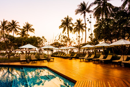 Silhouette coconut palm tree with umbrella and chair at sunrise time around outdoor swimming pool in hotel resort - Vintage filterのeditorial素材