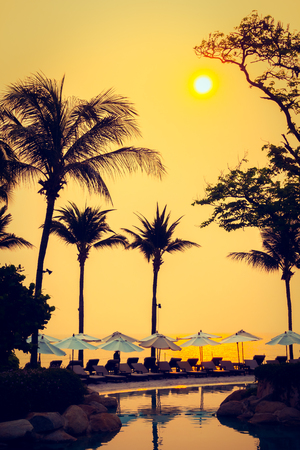 Beautiful Silhouette luxury umbrella and chair around swimming pool in hotel pool resort with coconut palm tree at sunrise times - Vintage Filter and Boost up color Processingのeditorial素材