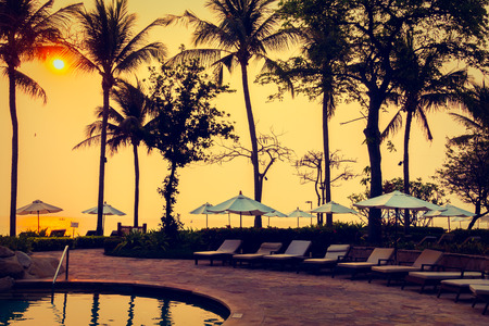 Beautiful Silhouette luxury umbrella and chair around swimming pool in hotel pool resort with coconut palm tree at sunrise times - Vintage Filter and Boost up color Processingのeditorial素材