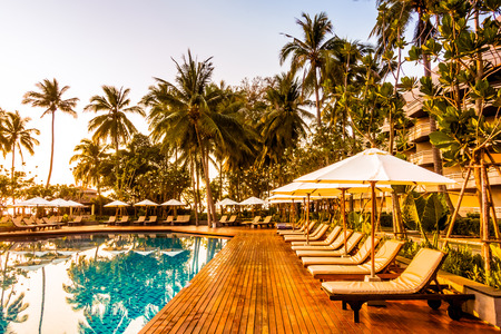 Silhouette coconut palm tree with umbrella and chair at sunrise time around outdoor swimming pool in hotel resort - Vintage filterのeditorial素材