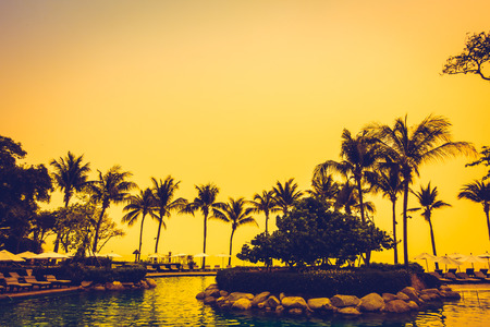 Beautiful Silhouette luxury umbrella and chair around swimming pool in hotel pool resort with coconut palm tree at sunrise times - Vintage Filter and Boost up color Processingのeditorial素材
