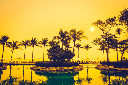 Beautiful Silhouette luxury umbrella and chair around swimming pool in hotel pool resort with coconut palm tree at sunrise times - Vintage Filter and Boost up color Processingの写真素材