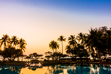 Silhouette coconut palm tree with umbrella and chair at sunrise time around outdoor swimming pool in hotel resort - Vintage filterのeditorial素材