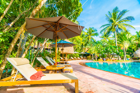 Umbrella and chair around outdoor swimming pool in hotel resort - Holiday vacation background concept - Boost up color Processingのeditorial素材
