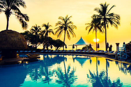 Beautiful luxury umbrella and chair and coconut palm tree around outdoor swimming pool in hotel resort at sunrise time - Vintage filter and boost up color Processingのeditorial素材