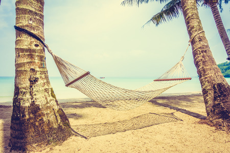 Empty hammock on beautiful tropical beach and sea with coconut palm tree - Boost up color Processing and Vintage Filterの写真素材
