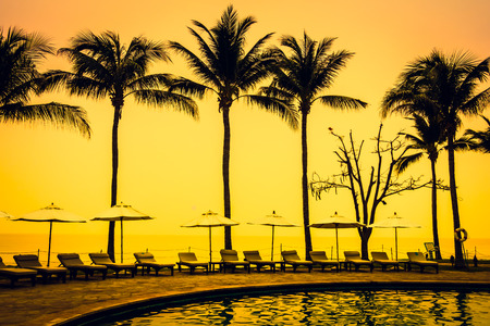 Beautiful Silhouette luxury umbrella and chair around swimming pool in hotel pool resort with coconut palm tree at sunrise times - Vintage Filter and Boost up color Processingのeditorial素材