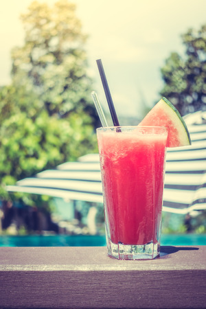 Watermelon juice in glass with beautiful luxury swimming in hotel background - Vintage Filter and Sunflare Processingの写真素材