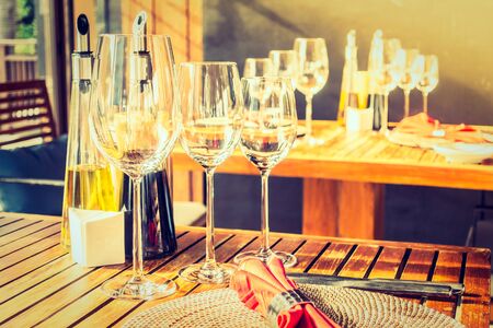 Selective focus point on wine glass with table setting for dinner in restaurant interior - Vintage Filter and Sunflare effectの写真素材