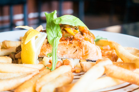 Selective focus point on Grilled salmon steak with french fries and lemon on white plateの写真素材