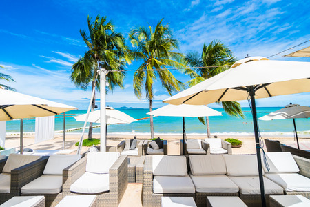 Umbrella and chair on the beautiful beach and sea with tropical palm tree on blue sky background