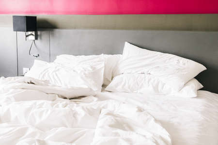 White pillow on messy and sheet bed decoration in bedroom interiorの写真素材