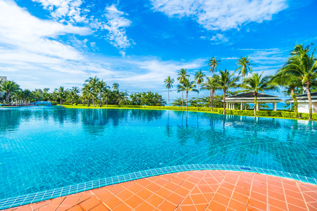 Beautiful luxury umbrella and chair around outdoor swimming pool in hotel and resort with coconut palm tree on blue sky - Boost up color Processingの写真素材